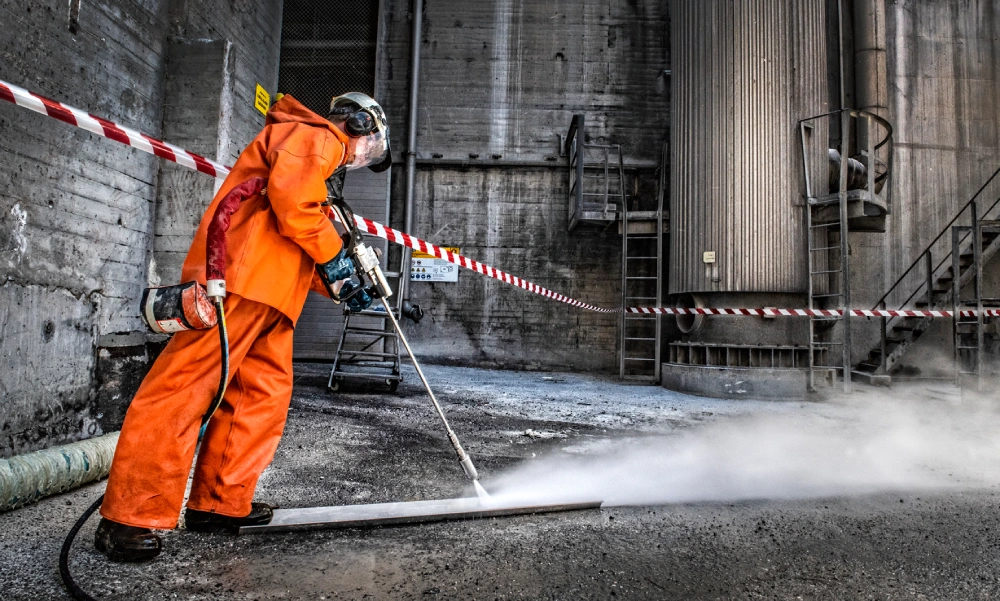 A worker in protective gear uses high-pressure water jetting to clean an industrial surface.