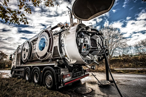 A Norva24 advanced vacuum truck in operation, extracting waste through hoses near an open manhole on a sunny day.