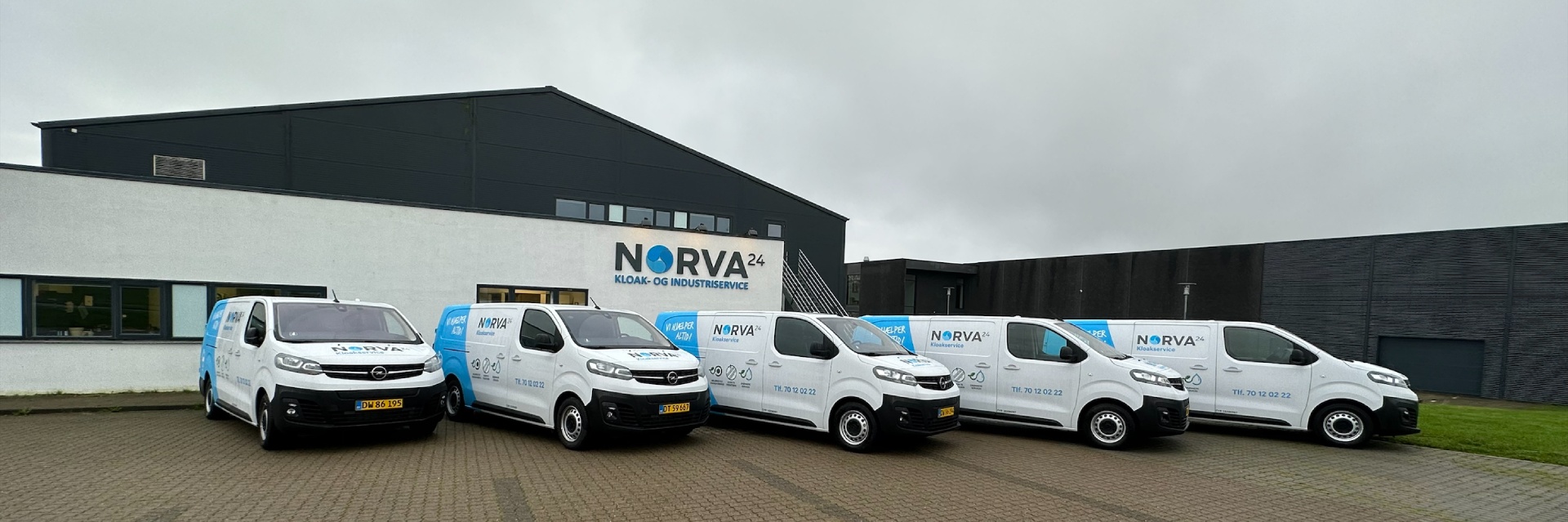 Five branded Norva24 service vans parked in front of a company building on a cloudy day.