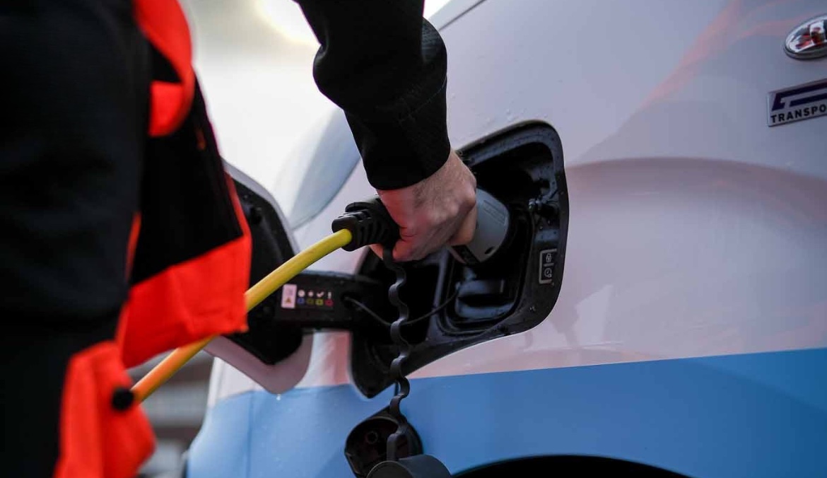 Person charging an electric vehicle with a yellow cable at a charging station.